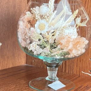 Composizione artigianale di fiori secchi e stabilizzati bianchi e rosa cipria in coppa di vetro con piede