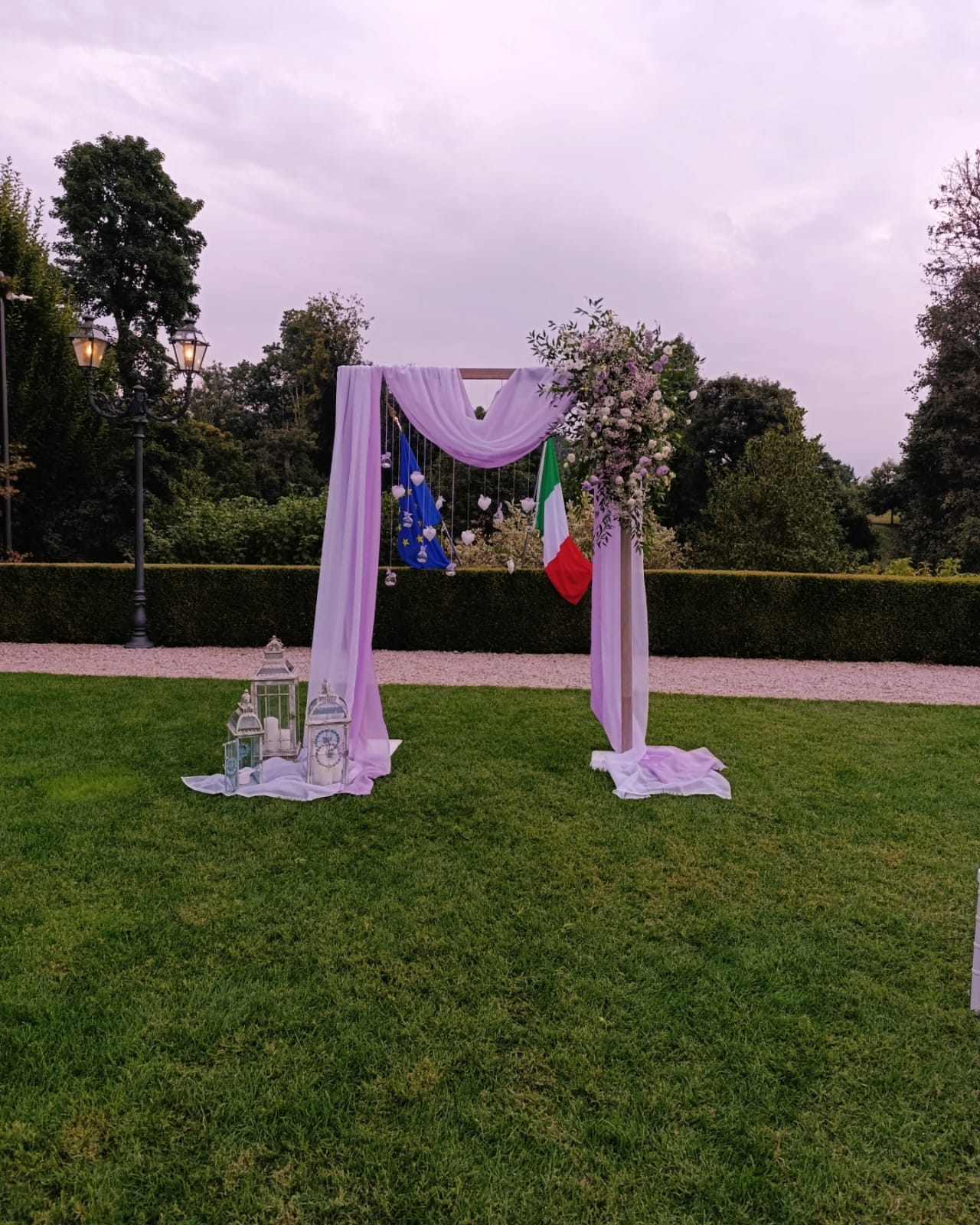 Arco della cerimonia con drappi lilla, fiori e lanterne nel giardino